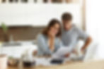 This photo shows a man and a woman standing in their kitchen, looking worried while studying some papers